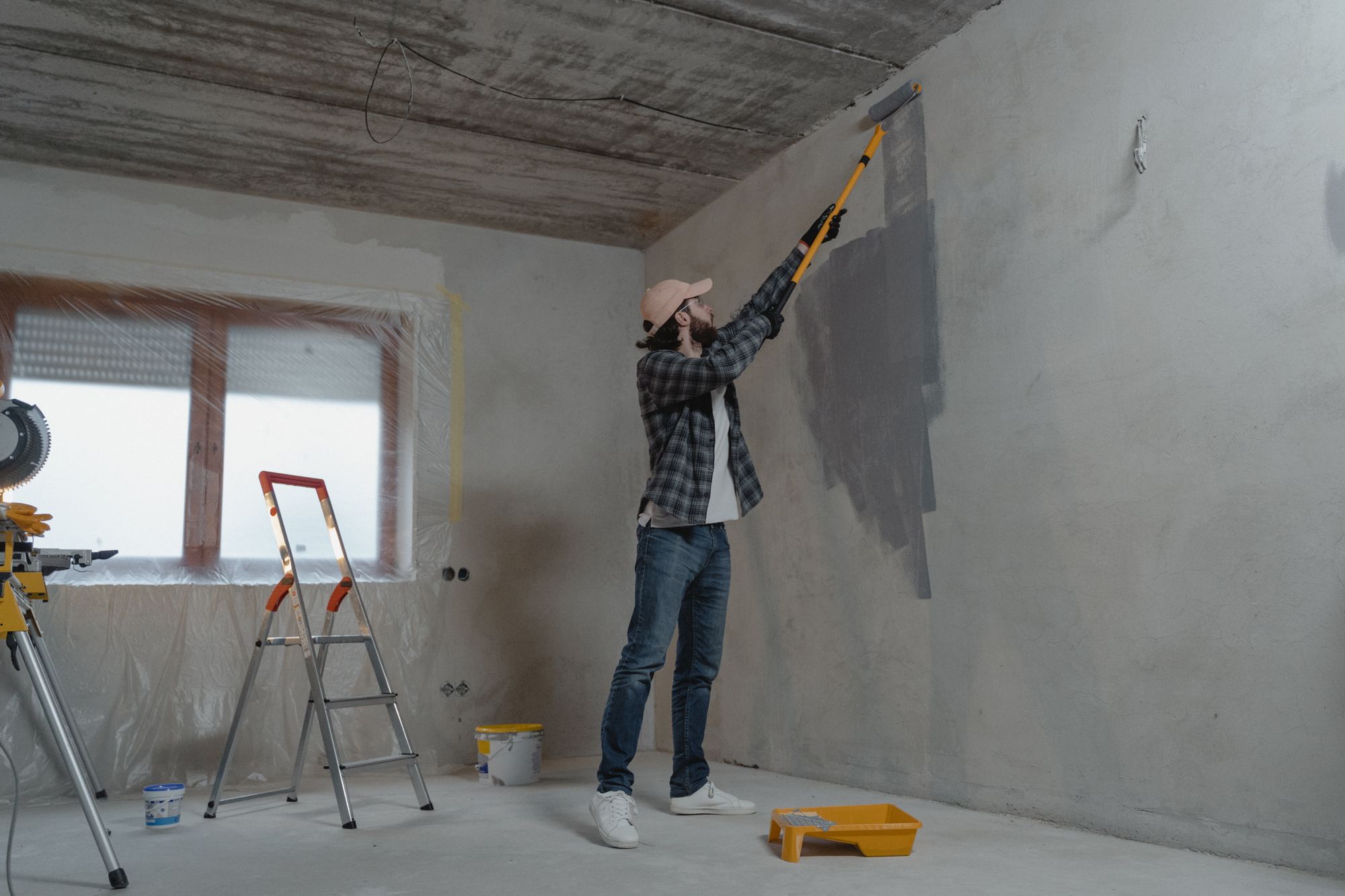 Schilder brengt grijze muurverf aan met een roller in een woning